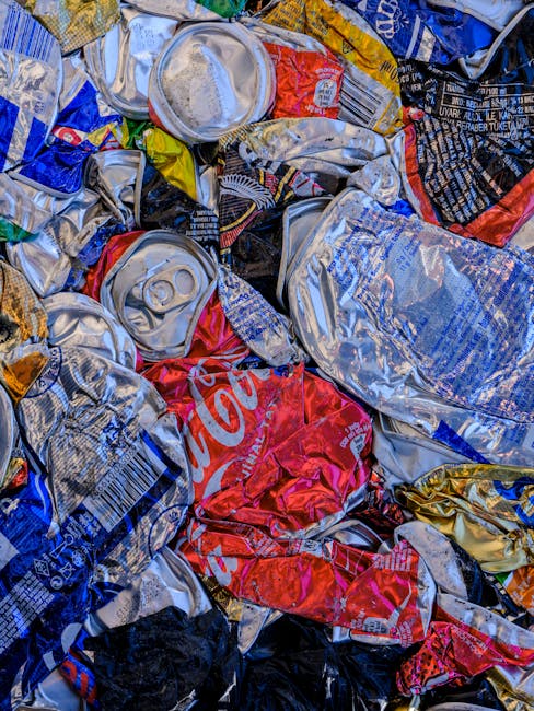 A person's arm and hand are visible, holding a green and blue tied plastic rubbish bag by its twisted top. The bag appears filled with waste materials, with some parts bulging slightly, and is made of