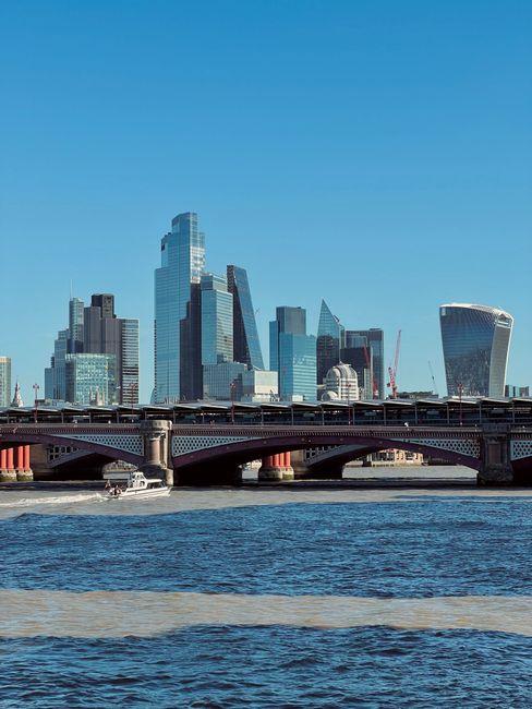 A daytime view of London’s financial district skyline featuring modern skyscrapers with glass and steel facades, including the prominent Walkie Talkie building on the right and the taller Tower in t