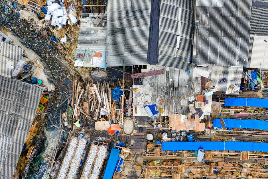 A narrow urban alleyway cluttered with piles of rubbish and discarded waste materials, including large bags filled with trash positioned in the foreground. The alley is flanked by brick and concrete b